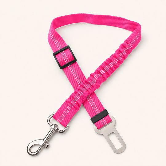 Pink SafeBelt adjustable dog car seat belt on a warm cream background